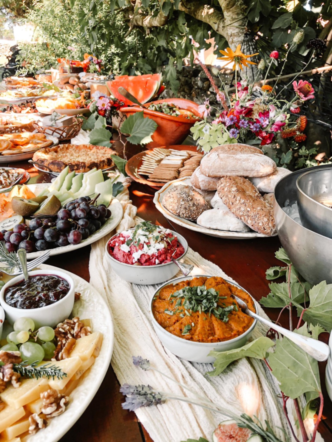 A long garden table laid with fresh breads, fruits, and wildflowers
